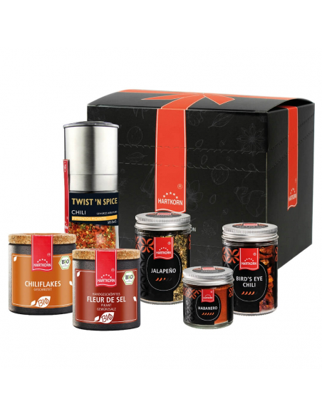 Schwarze Geschenkbox mit rotem Band, davor verschiedene Chilisalze, Flakes und Gewürze in unterschiedlichen Verpackungen. Schwarze Geschenkbox mit rotem Band, davor verschiedene Chilisalze, Flakes und Gewürze in unterschiedlichen Verpackungen.