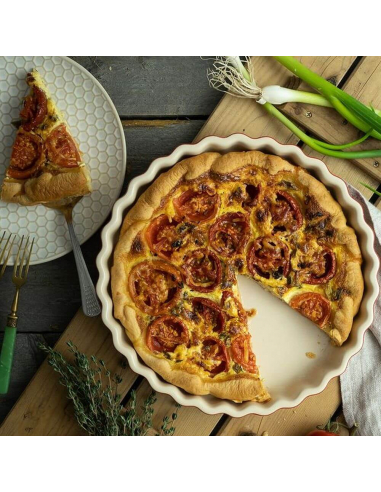 Aufgeschnittene Quiche mit Tomaten in Backform, daneben ein Teller mit einem Stück und Besteck.