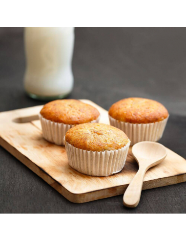 Drei Muffins in weißen Papierförmchen auf einem Holzbrett mit Holzlöffel und Milchflasche.