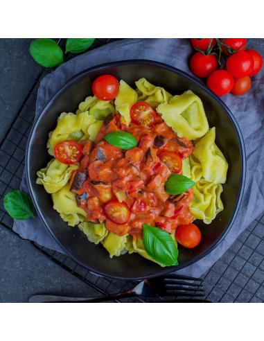 Schwarzer Teller mit Tortellini in roter Soße, dekoriert mit Basilikumblättern und frischen Tomaten.