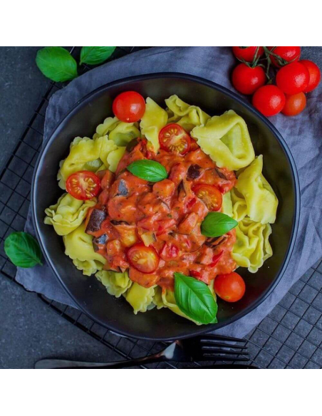 Schwarzer Teller mit Tortellini in roter Soße, dekoriert mit Basilikumblättern und frischen Tomaten. Schwarzer Teller mit Tortellini in roter Soße, dekoriert mit Basilikumblättern und frischen Tomaten.