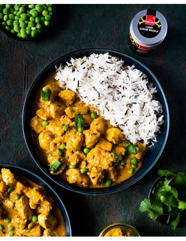 Indisches Curry mit Hähnchen, Erbsen und Basmati-Reis in schwarzer Schale, daneben Gewürzglas mit Curry Garam Masala