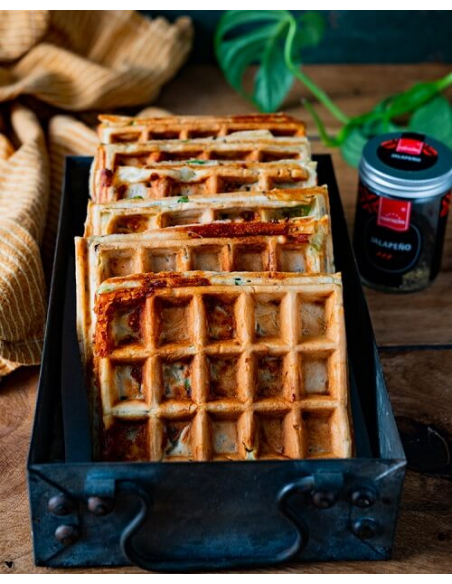 Jalapeño-Käse Waffeln - Herzhafte Waffeln mit Jalapeño in schwarzer Backform, im Hintergrund Glas mit Hartkorn-Logo Jalapeño-Käse Waffeln - Herzhafte Waffeln mit Jalapeño in schwarzer Backform, im Hintergrund Glas mit Hartkorn-Logo