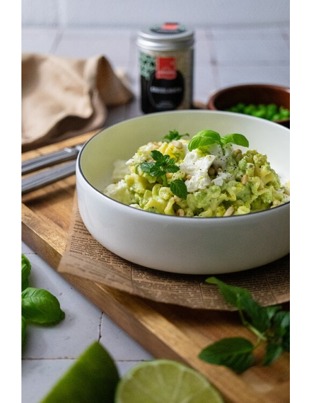 Cremiges Erbsenpesto-Pasta-Gericht mit Feta, Basilikum und Minze in weißer Schale, im Hintergrund gefriergetrockneter Knoblauch