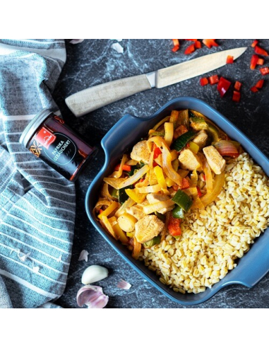 Paprika-Hähnchenpfanne mit Gemüse und Bulgur in blauer Form, daneben Glas mit Hartkorn-Logo und geräuchertem Paprikapulver