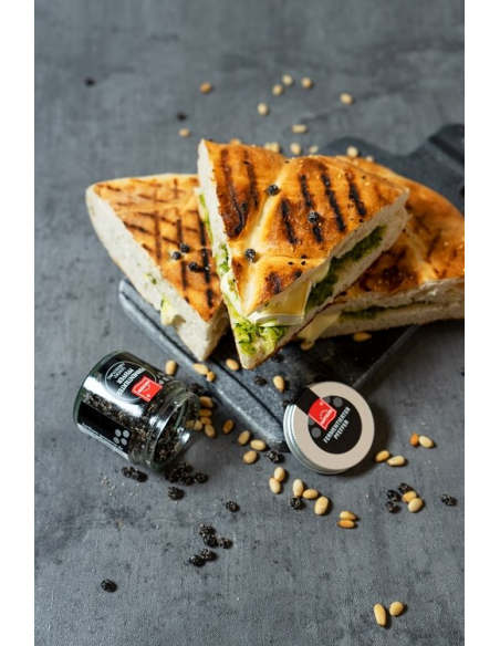 Gegrilltes Sandwich aufgeschnitten und serviert auf dunklem Brett, daneben offenes Glas mit Hartkorn fermentiertem Pfeffer