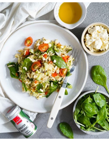 Teller mit Reissalat, Babyspinat, Tomaten und Feta, daneben kleine Schälchen mit Öl, Feta und Spinat, sowie ein Gewürzstreuer.