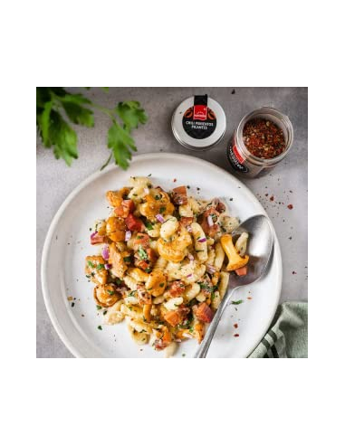 Pasta mit Speck, Zwiebeln und Chili-Gewürz auf weißem Teller, daneben Hartkorn Chili Pimientos Picantes