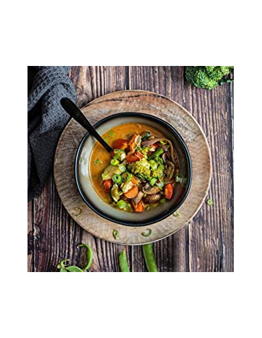 Asiatische Gemüsesuppe mit Brokkoli, Karotten, Pilzen und grünem Thai-Curry in schwarzer Schale auf Holzbrett