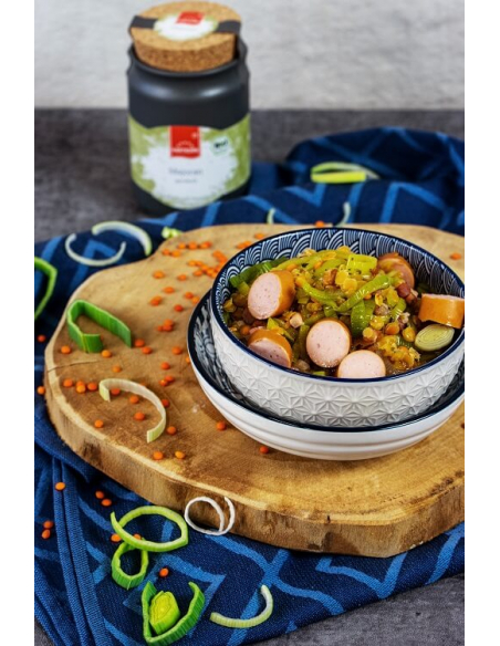 Linseneintopf mit Würstchen und Lauch auf einem Holzbrett angerichtet, im Hintergrund das Majoran-Keramiktöpfchen.