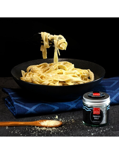 Abbildung Trüffelpasta im schwarzen Teller, vor dem Teller das Trüffelsalz im Glas. Moodbild