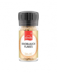 Kleine Gewürzmühle mit getrockneten Knoblauchflocken und schwarzem Drehverschluss, freigestellt auf weißem Hintergrund.