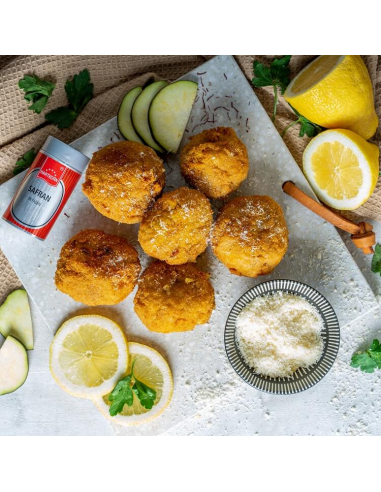 Gedeckter Tisch mit frittierten Bällchen, Zitronenscheiben, Zucchini und roter Safrandose im Hintergrund.