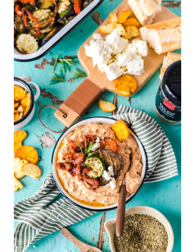 Schale mit cremigem Dip, getoppt mit gegrilltem Gemüse, Chips und Kräutern, daneben grün-weißes Tuch