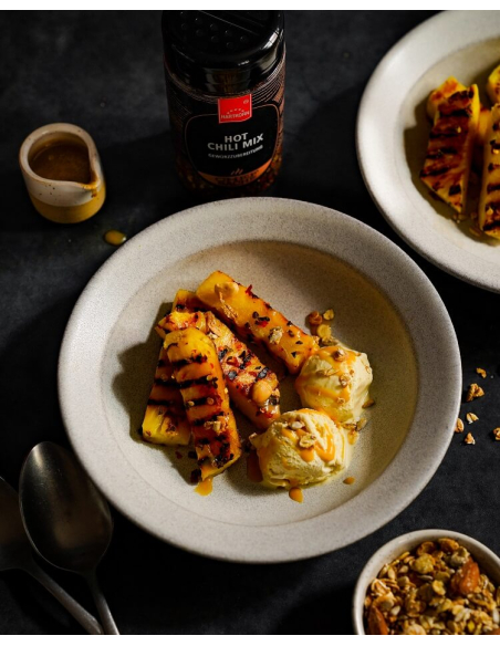 Gegrillte Ananasstücke mit zwei Kugeln Eis und gerösteten Nüssen auf einem weißen Teller Gegrillte Ananasstücke mit zwei Kugeln Eis und gerösteten Nüssen auf einem weißen Teller
