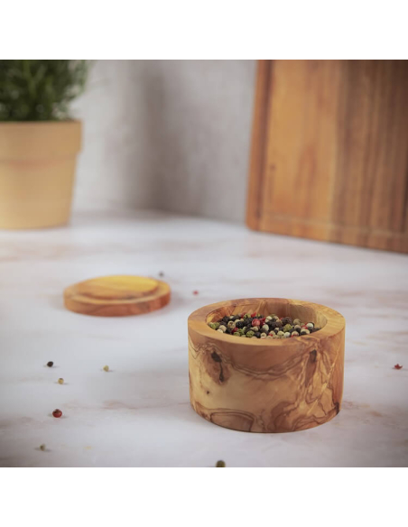 „Kleine geöffnete Dose aus Olivenholz, gefüllt mit Pfefferkörnern, steht auf heller Küchenplatte.