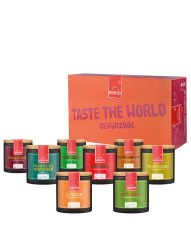 Acht schwarze Keramiktöpfchen mit bunten Etiketten vor einer orange-pinken Box mit der Aufschrift „Taste the World Gewürzbox“.