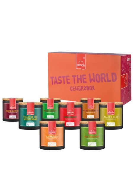 Acht schwarze Keramiktöpfchen mit bunten Etiketten vor einer orange-pinken Box mit der Aufschrift „Taste the World Gewürzbox“.