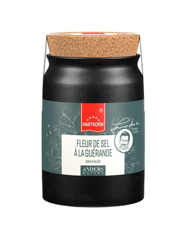 Schwarzes Keramiktöpfchen mit Korkdeckel. Gelbes Etikett mit rotem Band: ‚Fleur del Sel Gewürzsalz‘. BIO-Siegel sichtbar.