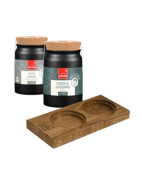 Zwei schwarze Keramiktöpfe mit Korkdeckeln davor liegt ein Holztablett mit zwei runden Aussparungen zur Präsentation der Töpfe.