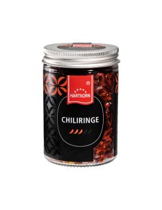 Glas mit getrockneten Chiliringen, silbernem Schraubdeckel und Etikett mit drei stilisierten Chilischoten als Schärfegrad