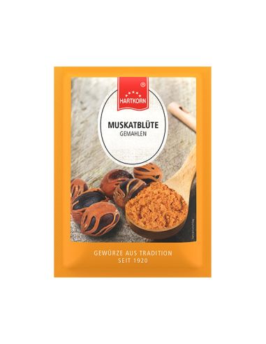 Flachbeutel mit gemahlener Muskatblüte, daneben Muskatblüten-Samen und ein Holzlöffel auf Holzuntergrund.