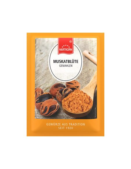 Flachbeutel mit gemahlener Muskatblüte, daneben Muskatblüten-Samen und ein Holzlöffel auf Holzuntergrund.