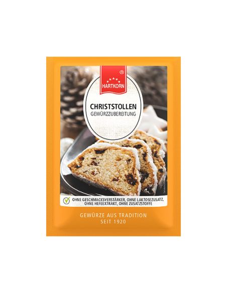 Flachbeutel mit der Aufschrift „Christstollen“, im Hintergrund angeschnittenes Gebäck und Zapfen auf dunklem Teller.