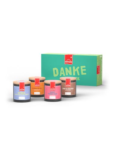 Grüne Geschenkbox mit rotem Etikett, der Schriftzug „DANKE GEWÜRZE“, davor stehen vier Pappdosen in verschiedenen Farben.