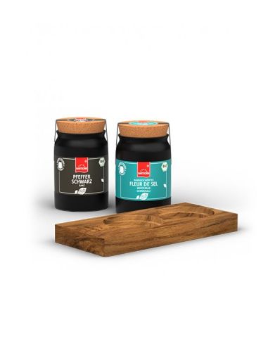 Zwei schwarze Keramiktöpfchen mit Etiketten „Fleur de Sel mediterran“ und „Pfeffer schwarz“ neben rechteckigen Servierholzbrett