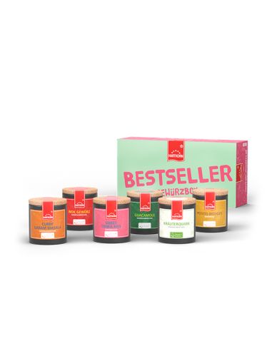 Mint-rosa Box mit der Aufschrift „Bestseller Gewürzbox“, davor sechs bunte Pappdosen mit Gewürzen.