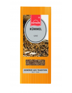 Flachbeutel mit der Aufschrift „Kümmel“, dahinter lose Kümmelsamen auf Holz.