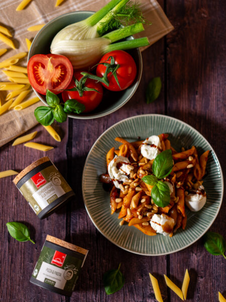 Pasta mit Tomaten, Mozzarella und Basilikum neben frischem Gemüse und Gewürzdosen