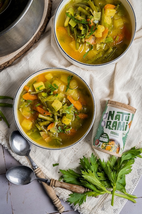 Klare Gemüsesuppe mit grünen Bohnen, Karotten und Kartoffeln in einer weißen Schale, daneben das Naturami Gewürzsalz Original