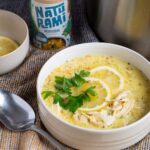 Eine gelbliche Suppe mit Zitrone und Hähnchen, im Hintergrund steht eine Dose Naturami mediterran.