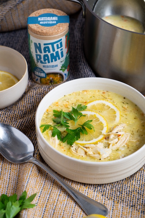 Eine gelbliche Suppe mit Zitrone und Hähnchen, im Hintergrund steht eine Dose Naturami mediterran.