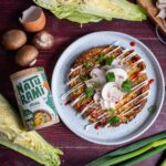 Ein vegetarisches Okonomiyaki auf einem Teller, getoppt mit Sesammayonnaise, Srirachasoße, Frühlingszwiebeln und frischem Koriander