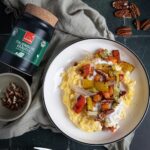 Teller mit cremiger Kokos-Polenta, getoppt mit geröstetem Gemüse und Pekannüssen, daneben Hartkorn Italienische Kräuter