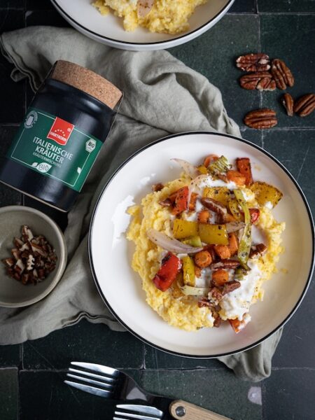 Teller mit cremiger Kokos-Polenta, getoppt mit geröstetem Gemüse und Pekannüssen, daneben Hartkorn Italienische Kräuter