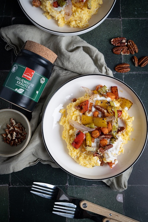 Teller mit cremiger Kokos-Polenta, getoppt mit geröstetem Gemüse und Pekannüssen, daneben Hartkorn Italienische Kräuter