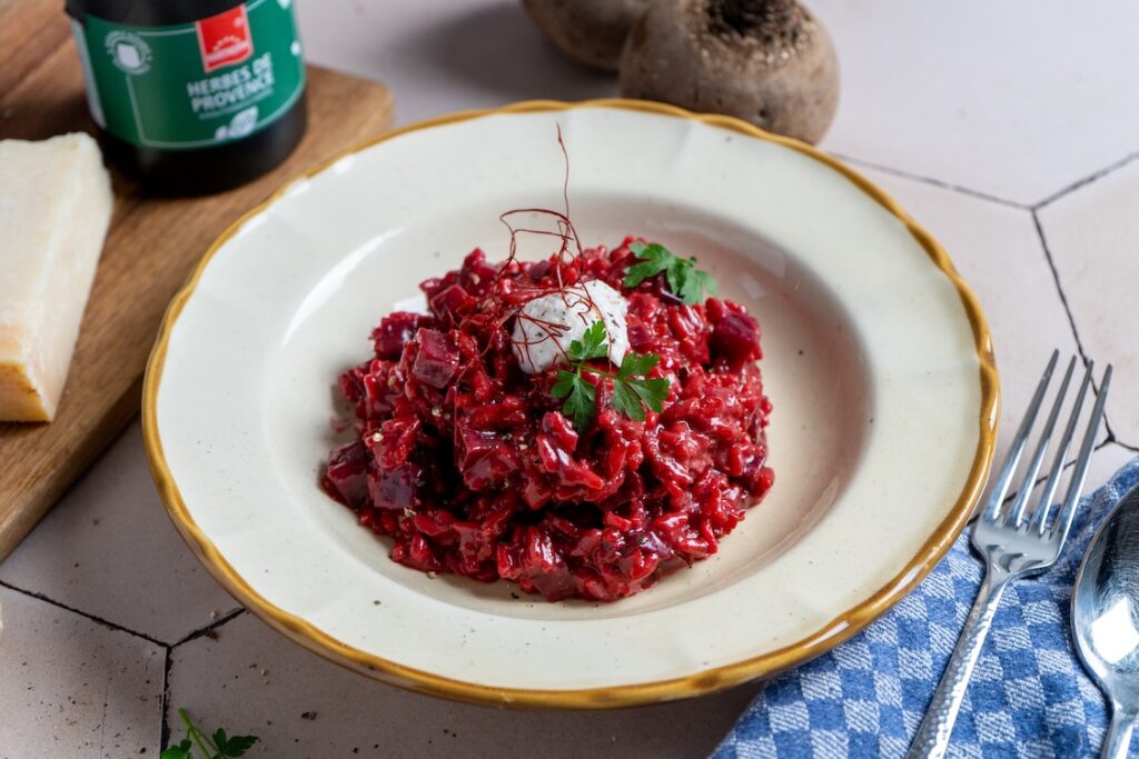 Rote-Bete-Risotto mit Meerrettich und Herbes de Provence, garniert mit Parmesan und Kräutern in einem tiefen Teller