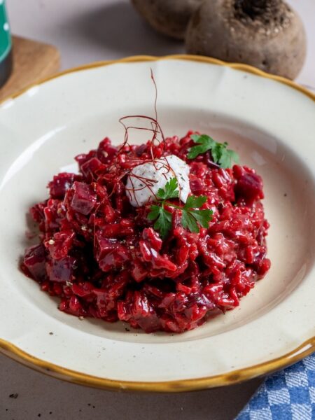 Rote-Bete-Risotto mit Meerrettich und Herbes de Provence, garniert mit Parmesan und Kräutern in einem tiefen Teller
