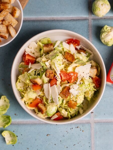 Winter-Caesar-Salat mit Rosenkohl, Parmesan, Croûtons und Chili-Knoblauch-Dressing in einer Schüssel angerichtet