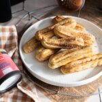 Goldbraune Churros aus der Heißluftfritteuse auf einem weißen Teller, daneben Sweet Tonka Kiss Gewürzzucker von Hartkorn.