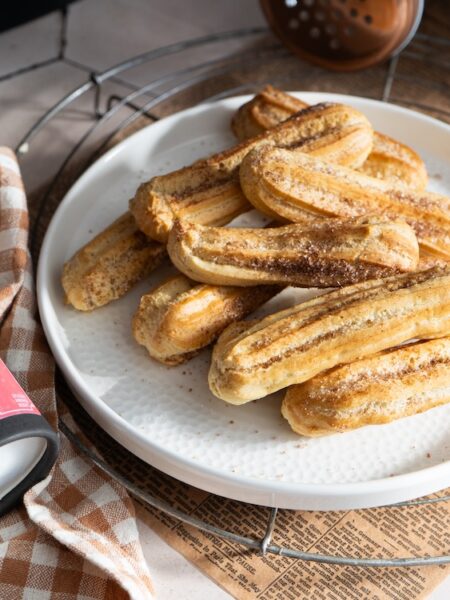 Goldbraune Churros aus der Heißluftfritteuse auf einem weißen Teller, daneben Sweet Tonka Kiss Gewürzzucker von Hartkorn.